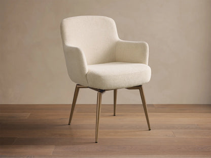Front view of the cream upholstered Willem Dining Arm Chair with curved back, armrests, and antique brass finish metal legs.