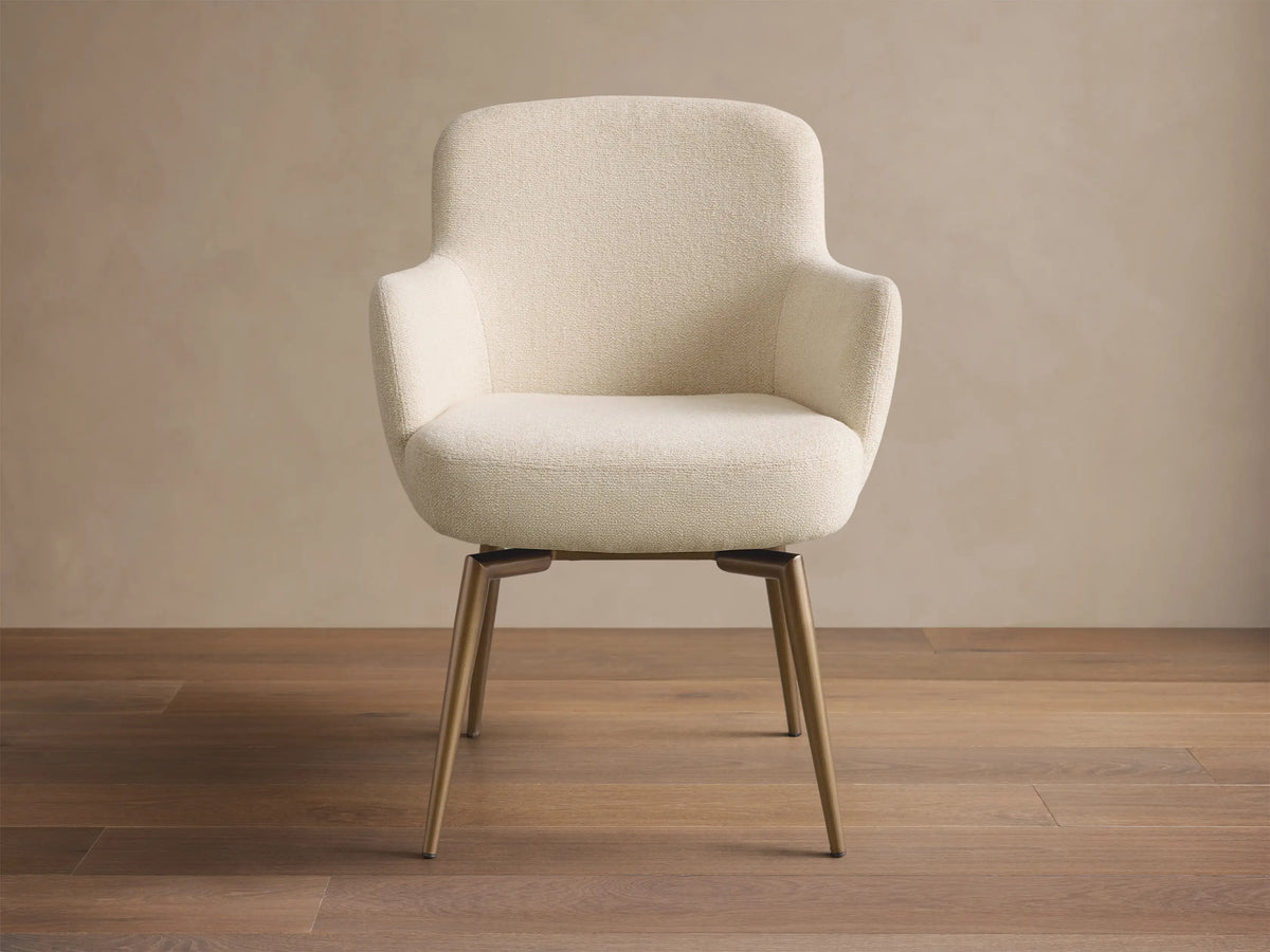 Front view of the cream upholstered Willem Dining Arm Chair with curved back, armrests, and antique brass finish metal legs.