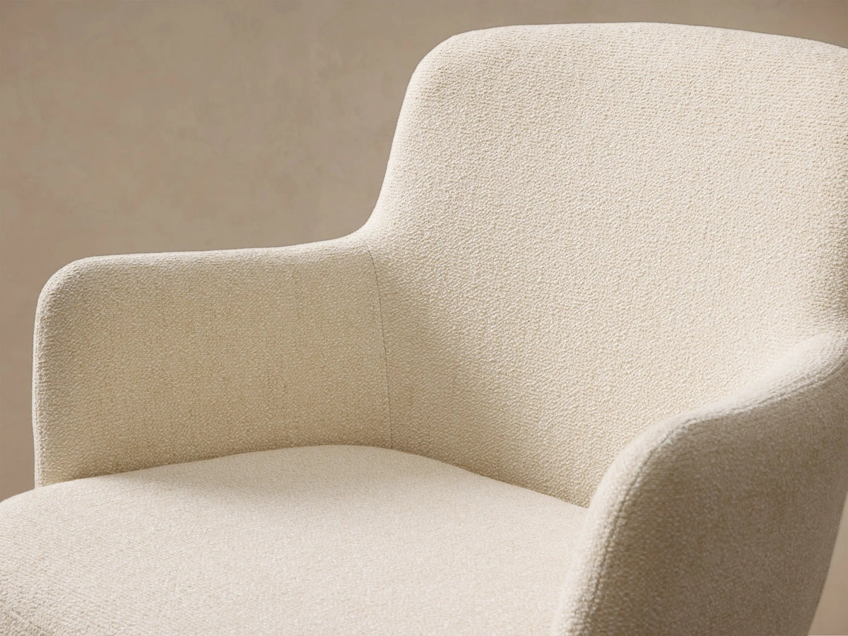 Front view of a cream upholstered Willem Dining Arm Chair with curved armrests and antique brass tapered metal legs.