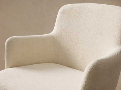 Front view of a cream upholstered Willem Dining Arm Chair with curved armrests and antique brass tapered metal legs.