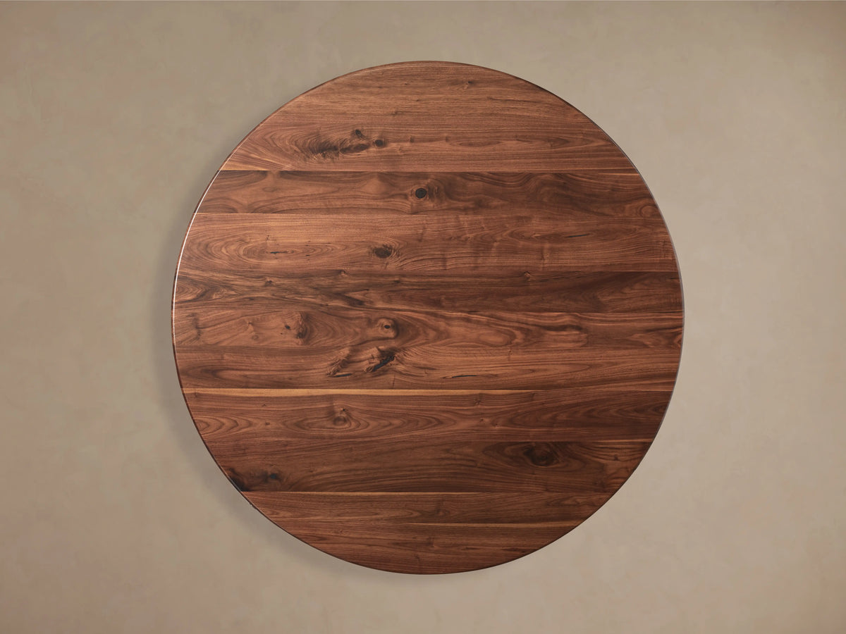 Round Jacob dining table with a smooth walnut tabletop displaying natural wood grains and knots, set against a neutral background.