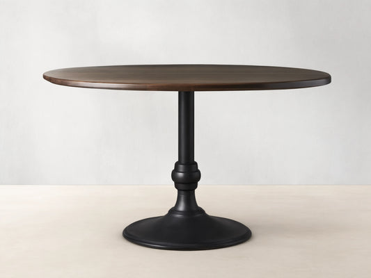 Jacob Round Dining Table with a dark wood tabletop and black cast iron base featuring a brass finish, on a wooden floor.