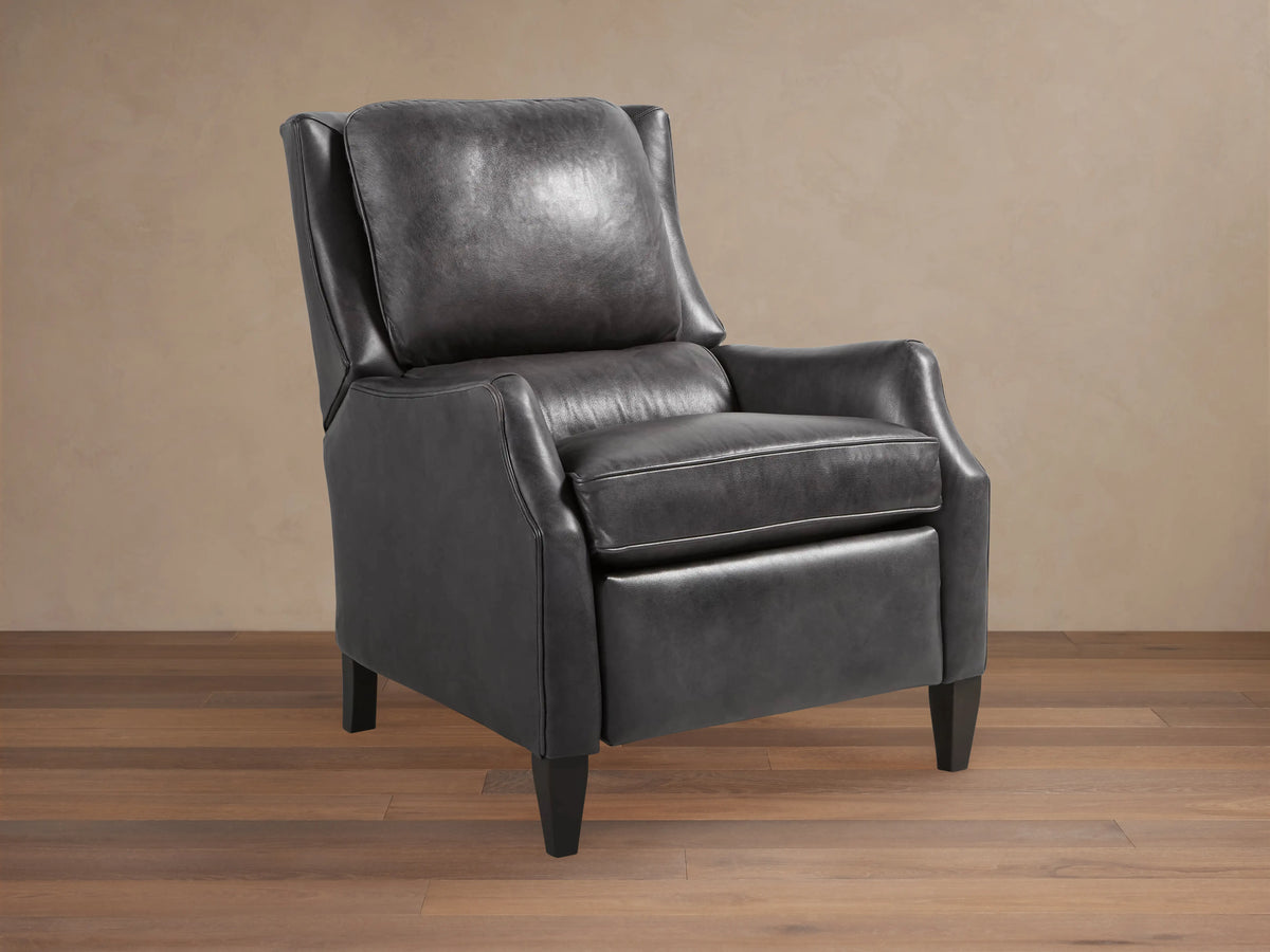 Alex Leather Recliner, dark gray, angled front-right. Features wingback design, contrast piping, tapered dark wood legs, on wood floor.