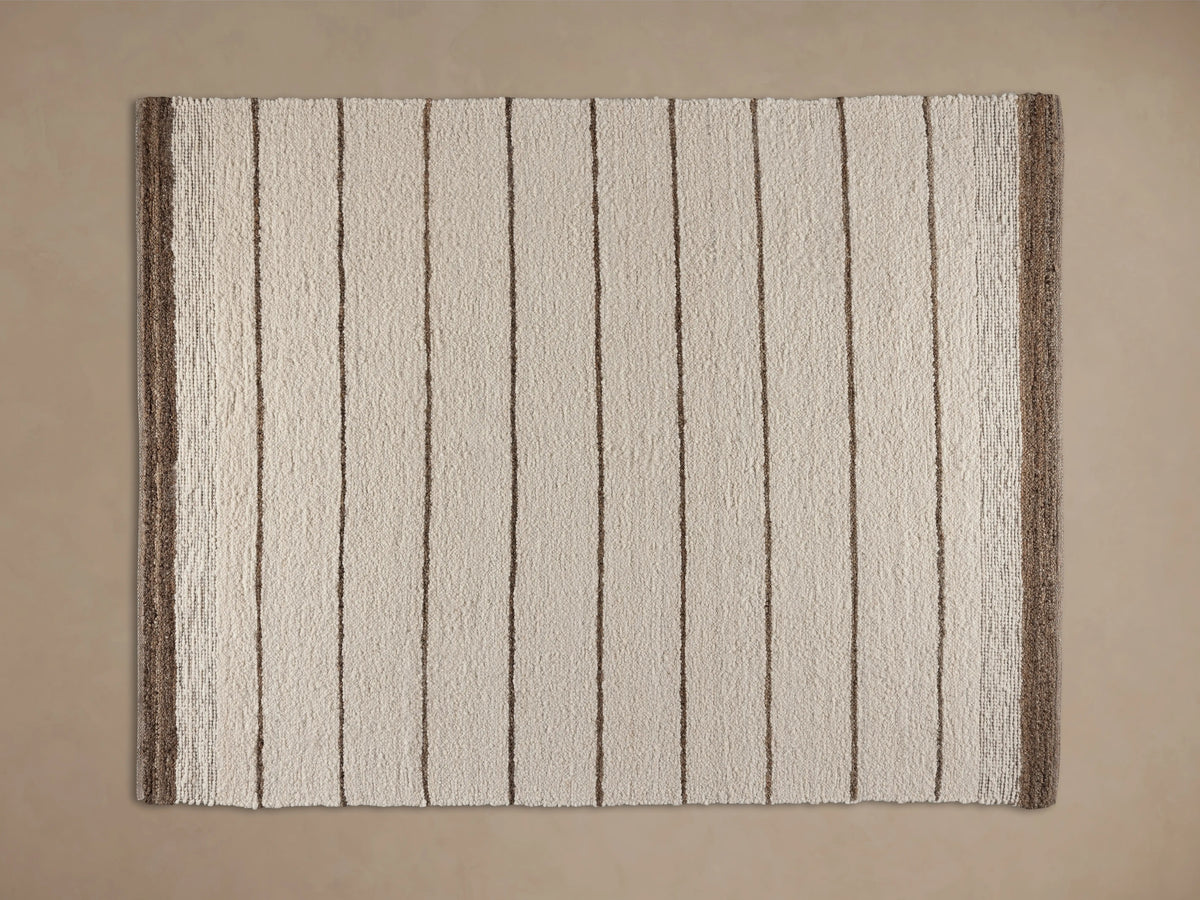 Alice Performance Rug: textured cream-colored rug with horizontal tan stripes and a thick dark brown border, on a wood floor.