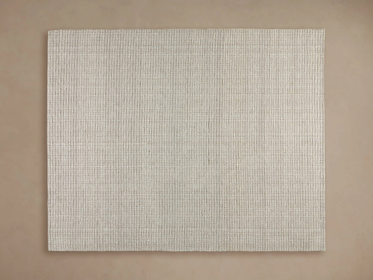 Dover Performance Rug in light beige with horizontal textured lines, partially beneath a wooden coffee table on a wood floor.