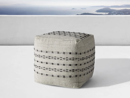 Ladera Performance Pouf, gray with black dotted and striped patterns, cubic shape, placed on wooden floor against beige background.