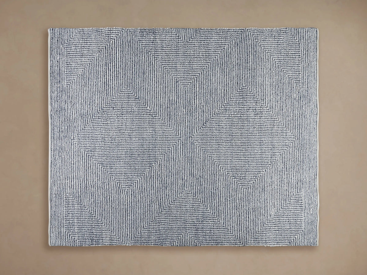 Maddux Performance Rug: light blue & white geometric striped pattern, handwoven texture, partially under wood furniture.