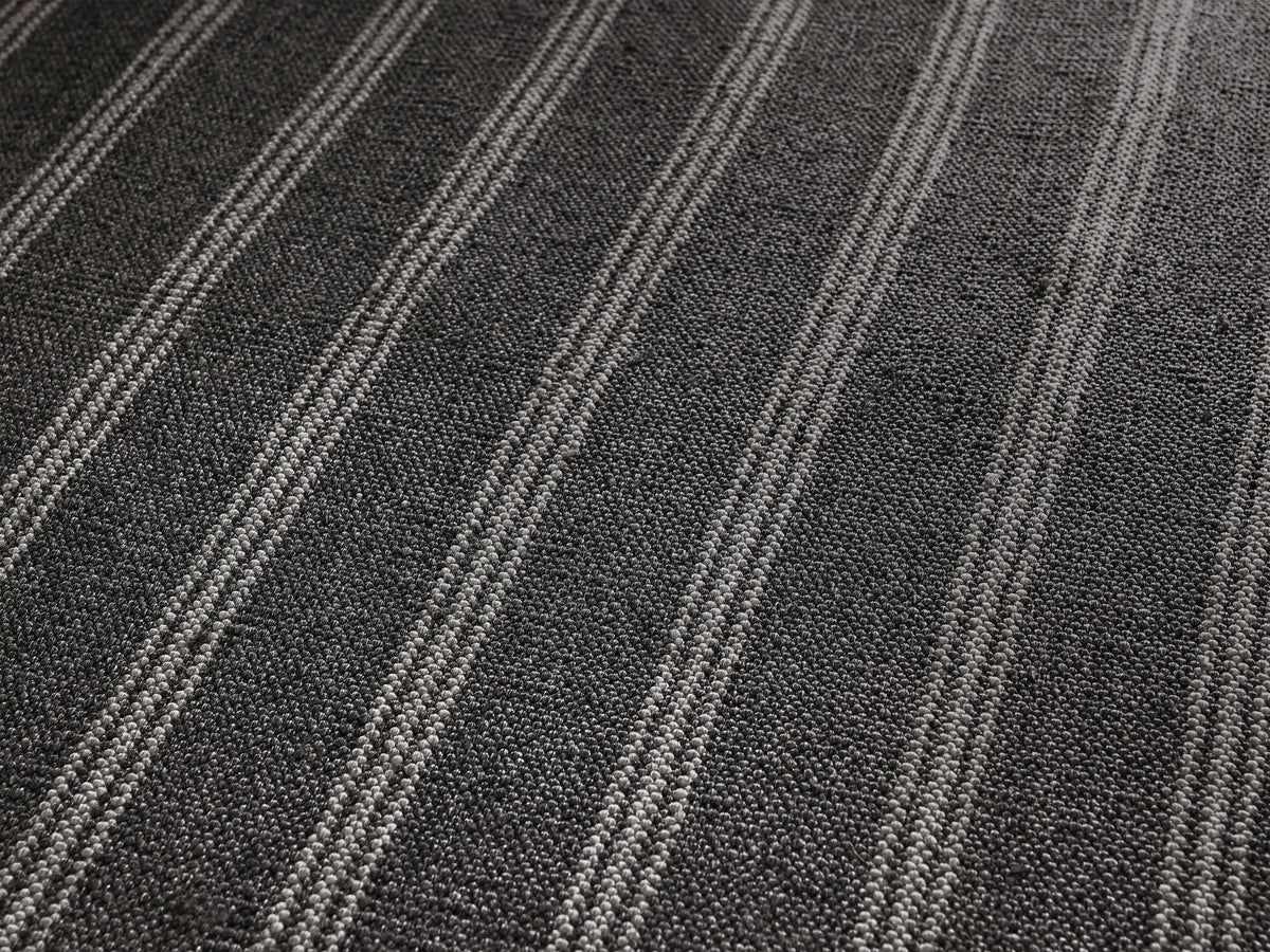 Grover Performance Rug: square, charcoal with thin white vertical stripes, laid flat on a light brown textured surface.