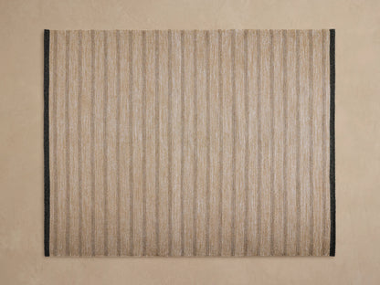 Grover Performance Rug, natural tan woven with thin dark gray horizontal stripes and a dark border, angled view.