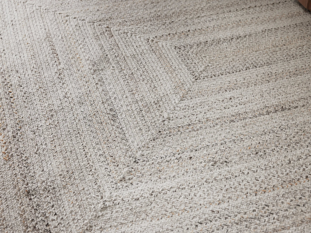 Sansa Performance Rug, light gray rectangular braided rug with concentric rectangle pattern, flat lay on a beige surface.