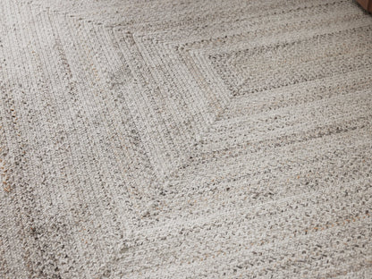 Sansa Performance Rug, light gray rectangular braided rug with concentric rectangle pattern, flat lay on a beige surface.