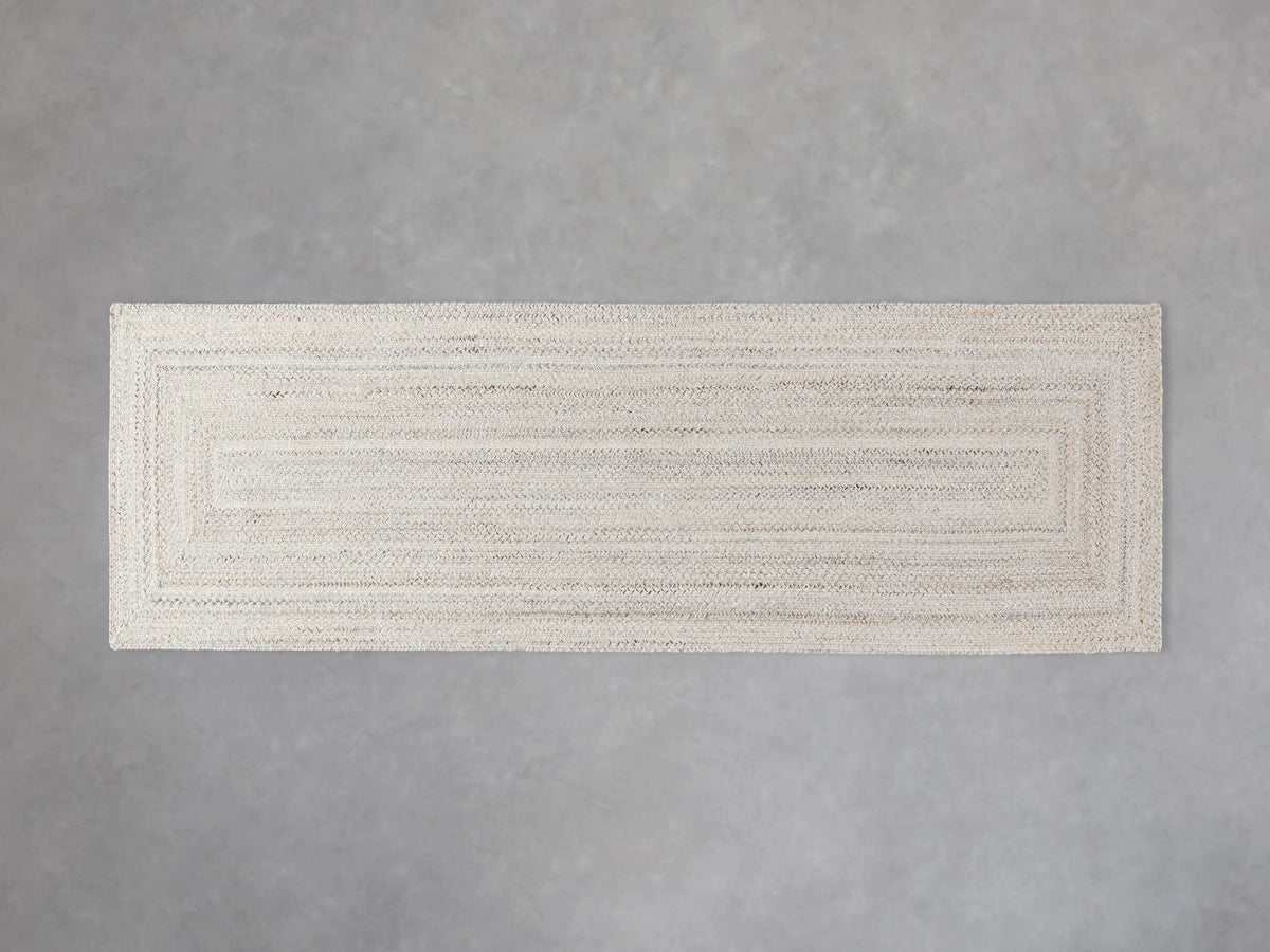 Sansa Performance Runner Rug, light rectangular braided rug with subtle inner rectangular border, on a gray floor.