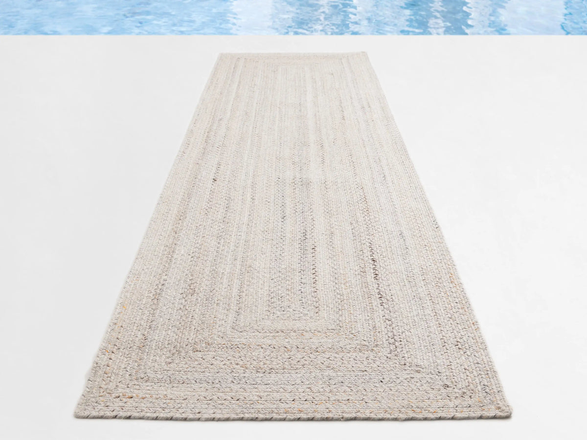 Long rectangular Sansa Performance Runner Rug, light cream braided texture with distinct woven border, on a white surface.