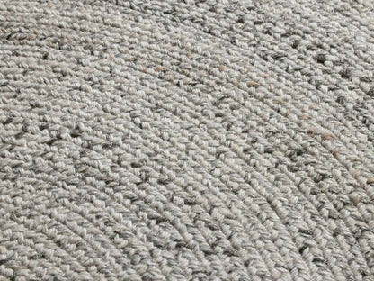 Sansa Performance Round Rug, a round braided rug with light off-white and grey concentric circles, on a tan floor.