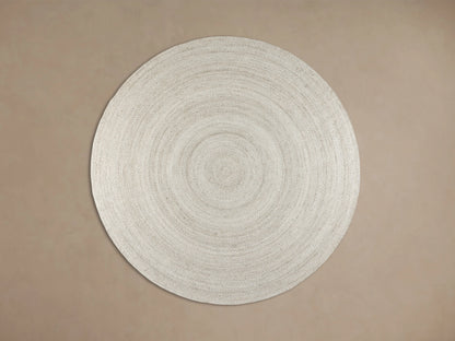 Sansa Performance Round Rug, natural braided with concentric circles, partly under black furniture on wood floor.