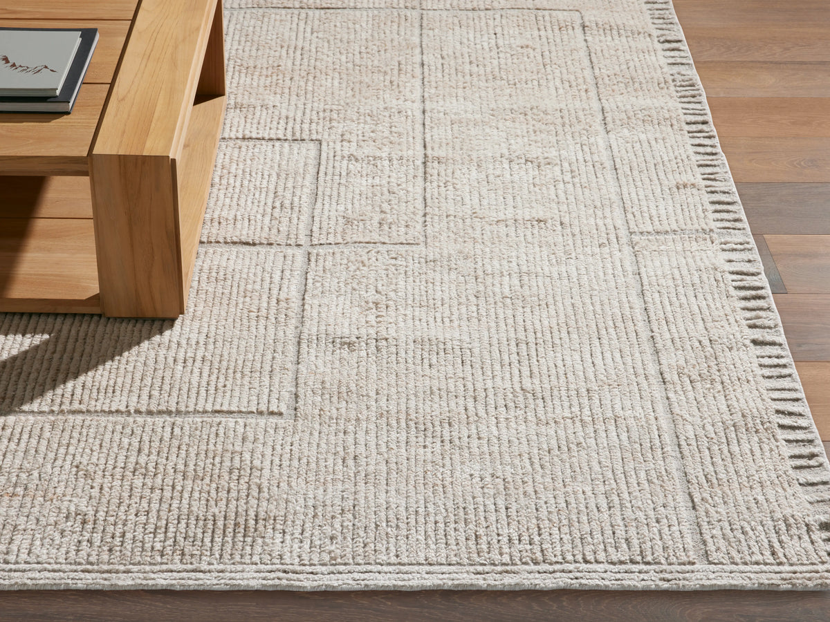 Close-up of a light beige Walker Performance Rug with raised linear and geometric patterns, partially under a wooden table on a wood floor.