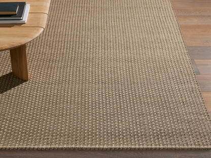 Hatcher Performance Rug with dense beige & brown weave, on a dark wood floor, partially under a light wood coffee table.