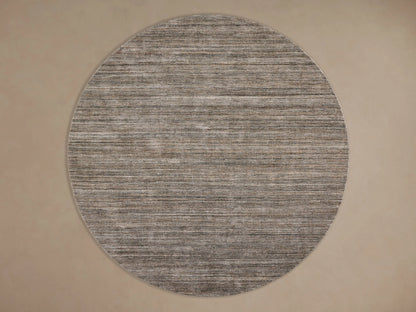 Textured round rug with horizontal stripes in multi-tone gray and brown on a dark wood floor, with a dark coffee table partially visible.
