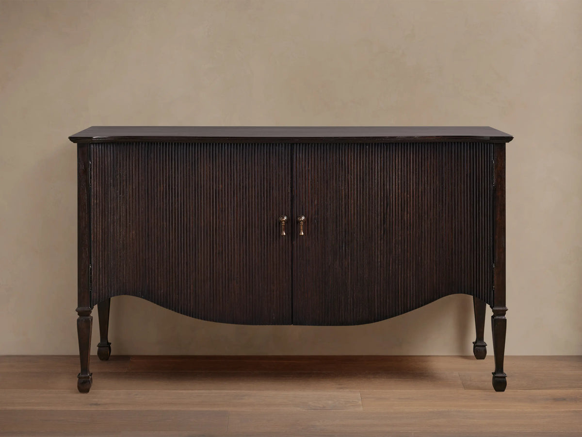 Dark brown Conrad Sideboard, front view, with fluted doors, brass knobs, curved base, and turned legs.