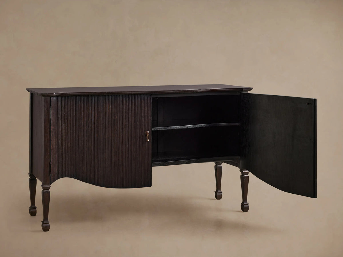 Dark brown Conrad Sideboard, front view, with fluted doors, brass knobs, curved base, and turned legs.