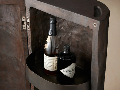 Open Log Bar made from dark reclaimed wood, showing 3 metal shelves filled with bottles & glasses against a brown wall.