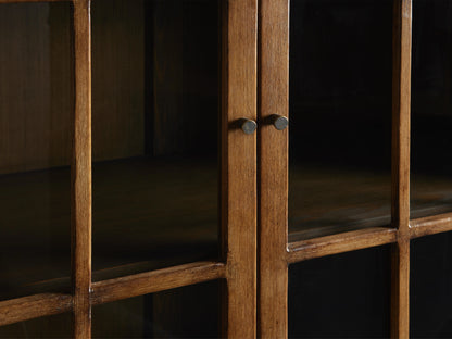 Close-up of Merritt Cabinet showing hand-painted distressed wood with subtly antiqued brass knobs. Visible glass paneled doors.