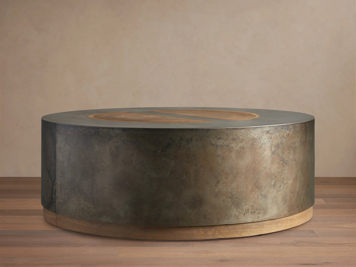 Round coffee table with a dark oxidized steel body and light wood accents. Top features concentric veneer circles from reclaimed wood.