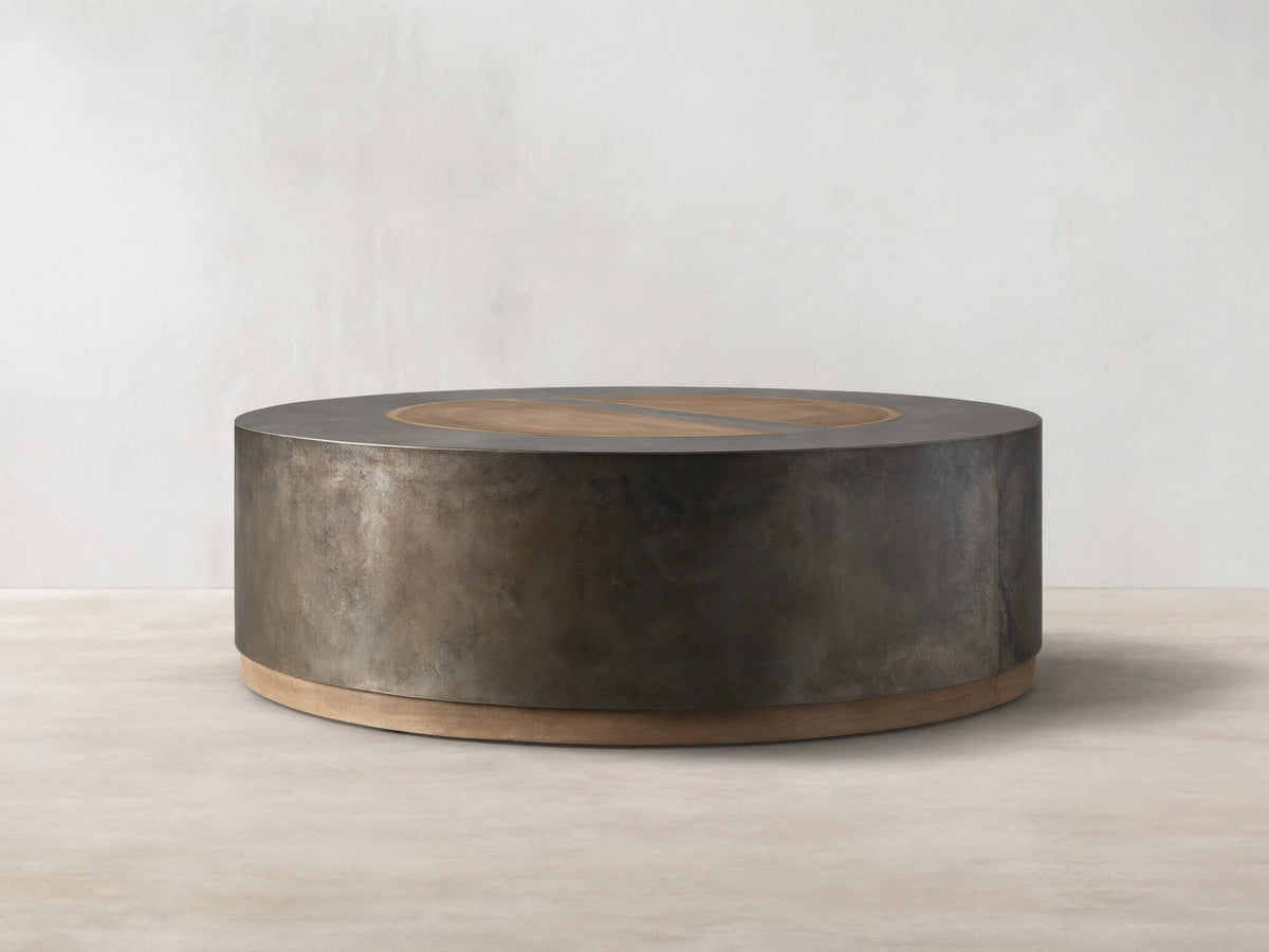 Round coffee table with a dark oxidized steel body and light wood accents. Top features concentric veneer circles from reclaimed wood.