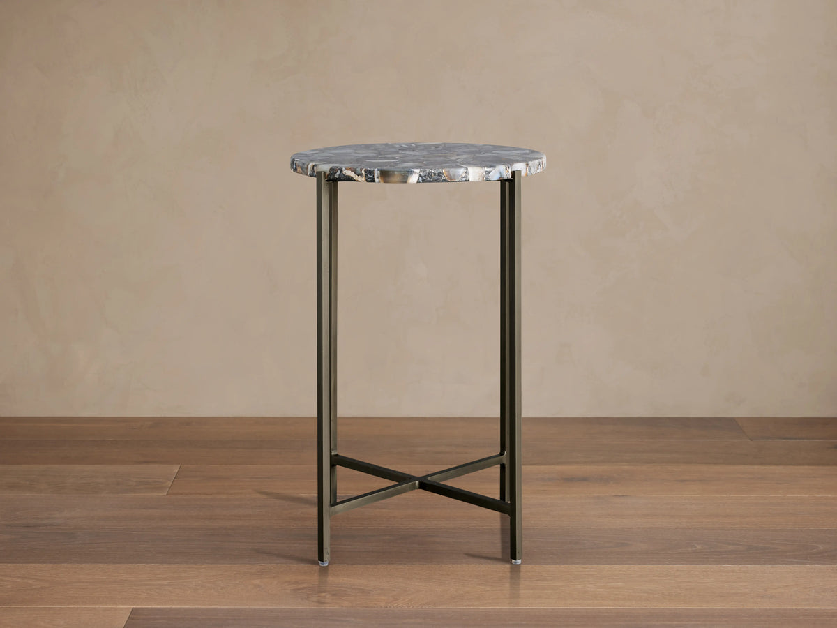 Ludlow Martini Table with a round stone top and thin iron legs, featuring an X-shaped base on a wooden floor.