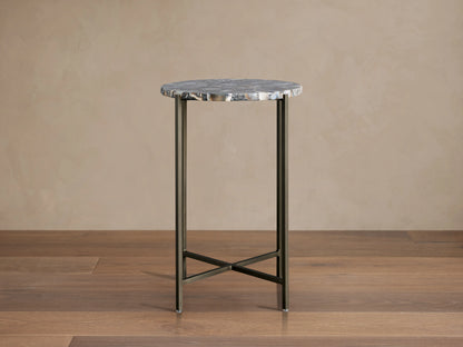 Ludlow Martini Table with a round stone top and thin iron legs, featuring an X-shaped base on a wooden floor.