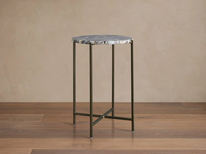 Ludlow Martini Table with a round, polished stone top and slender, hand-welded iron legs, on a wooden floor background.