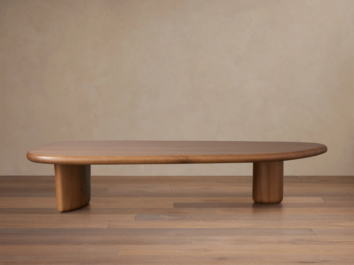 Akiro Coffee Table made from solid oak wood with a rounded edge. Features a smooth surface and cylindrical legs, set on wooden floor.