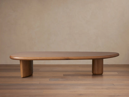 Akiro Coffee Table made from solid oak wood with a rounded edge. Features a smooth surface and cylindrical legs, set on wooden floor.