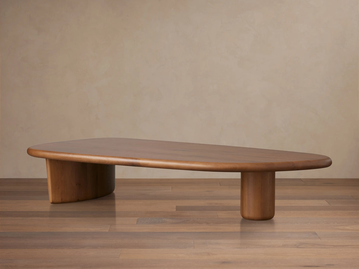 Front view of the solid oak Akiro Coffee Table, featuring a rounded oval top and sturdy base, styled with books and a vase.