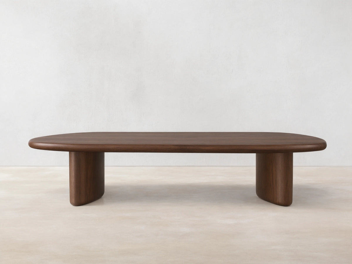 Akiro Coffee Table made from solid oak wood with a rounded edge. Features a smooth surface and cylindrical legs, set on wooden floor.
