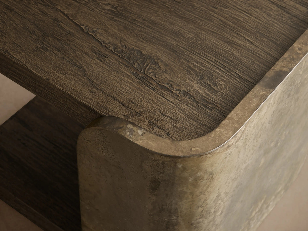 Alvaro End Table, C-shaped with dark spalted wood shelves & weathered, mottled bronze aluminum side panel on wood floor.