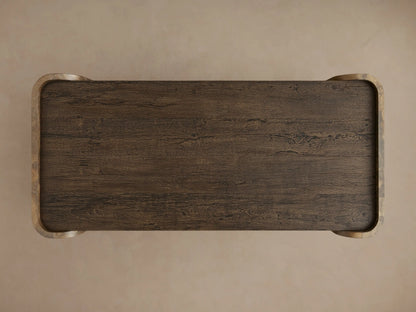 Close-up of Alvaro Coffee Table. Dark brown spalted primavera wood top & shelf with grain, connected by curved weathered aluminum panel with mottled bronze/gold patina.