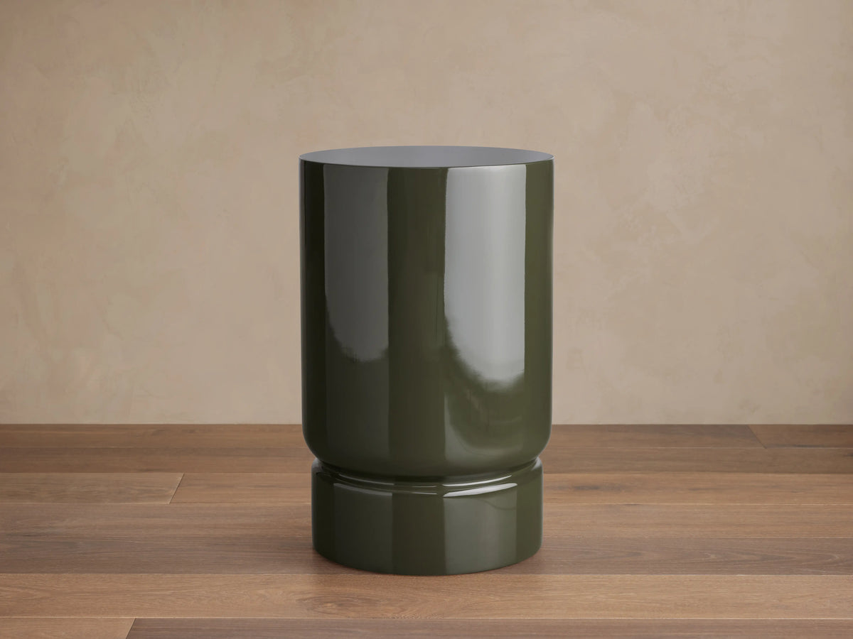 Alwyn Lacquer Stool in dark green finish, glossy cylindrical shape with a slightly wider base, placed on wooden floor.