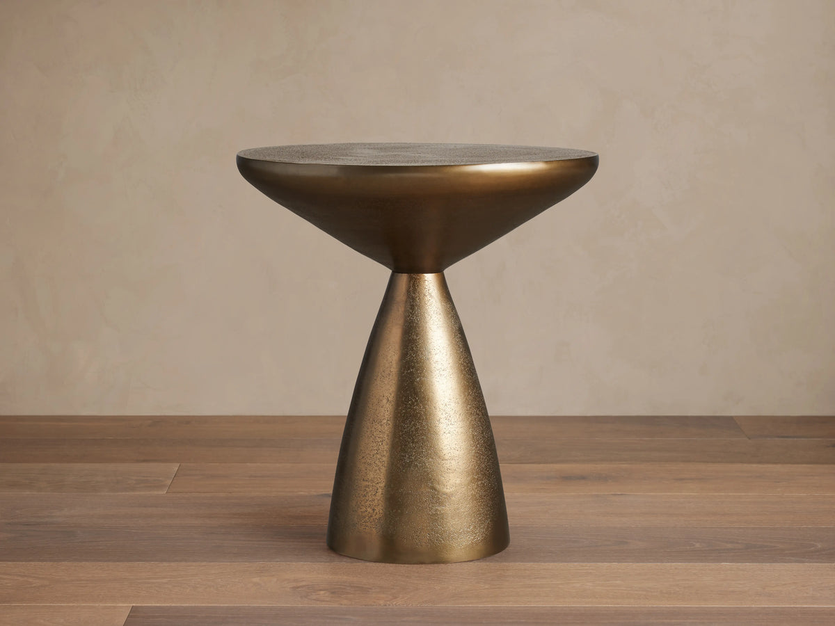 Amina End Table in polished bronze finish, featuring an inverted cone top and tapered base, placed on wood floor.