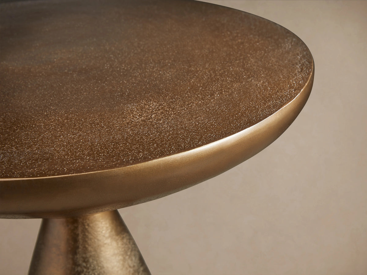 Amina End Table in polished bronze finish, featuring an inverted cone top and tapered base, placed on wood floor.