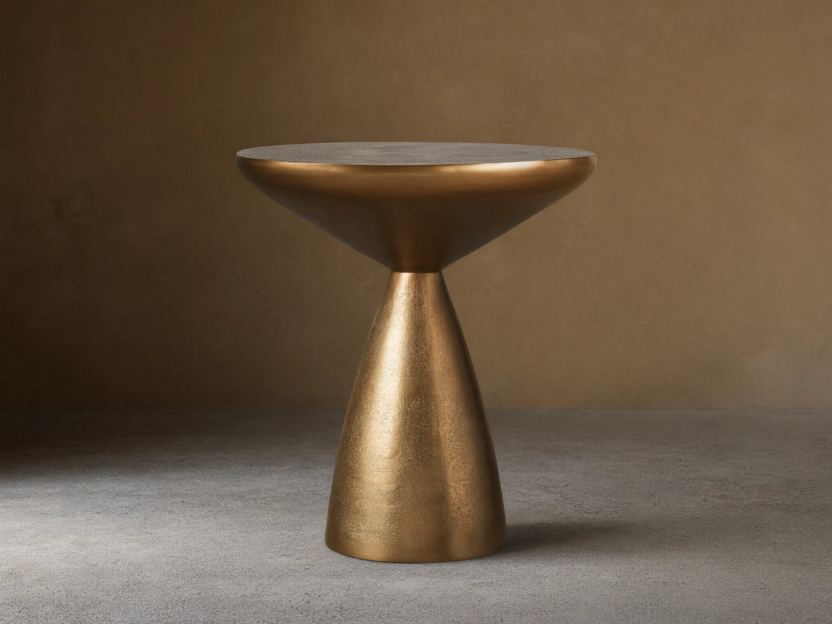 Amina End Table in polished bronze finish, featuring an inverted cone top and tapered base, placed on wood floor.
