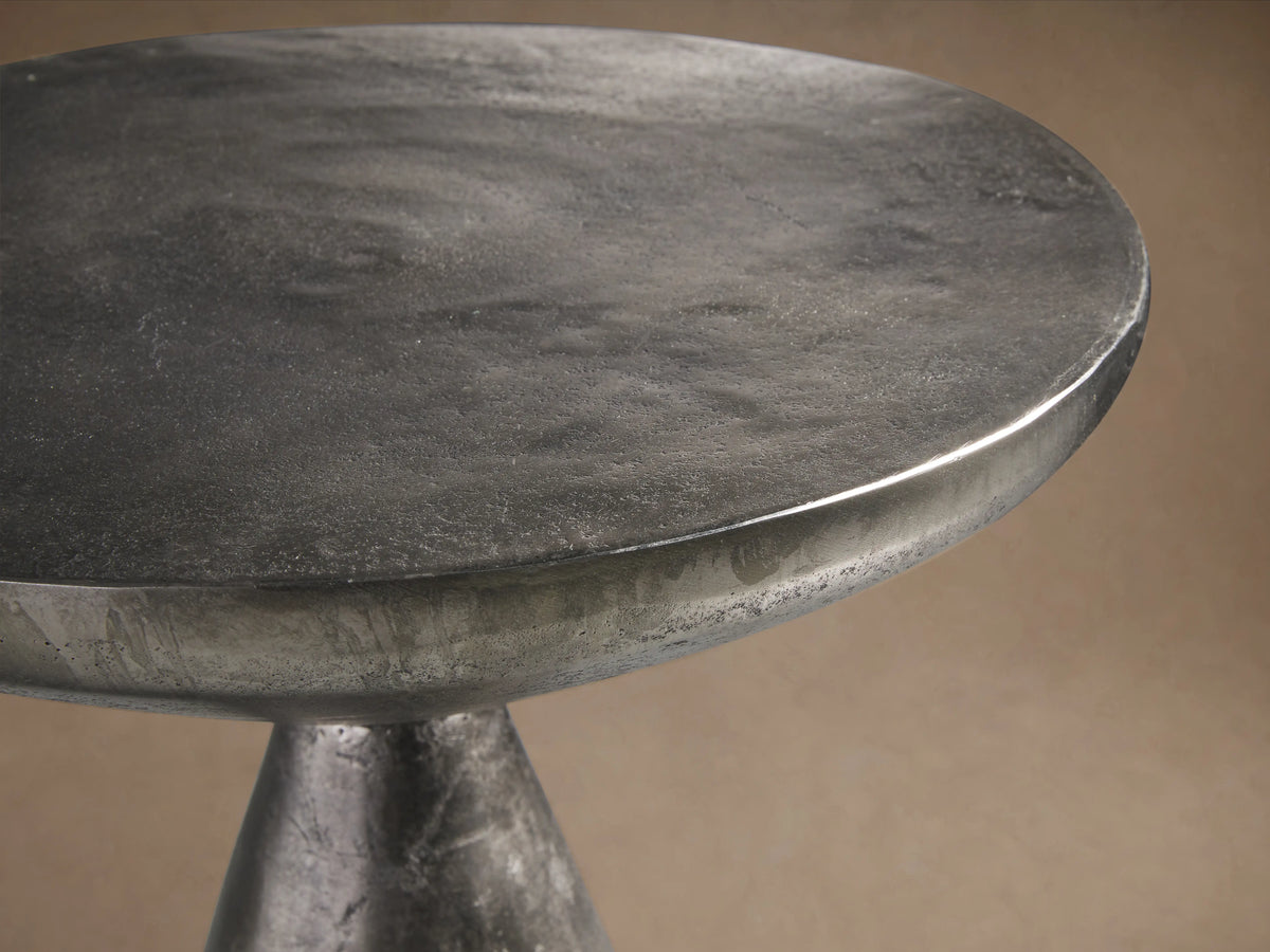 Amina End Table in splash nickel finish, showing a sleek, reflective surface with a modern, hourglass shape on a wooden floor.