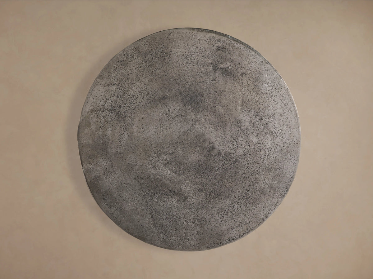 A close-up of the Amina End Table features a round, nickel-plated aluminum surface with a subtle drip finish, showcasing contemporary style.