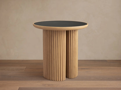 Astor Round End Table with a black marble tabletop and cylindrical oak reed-wrapped base on a wooden floor.