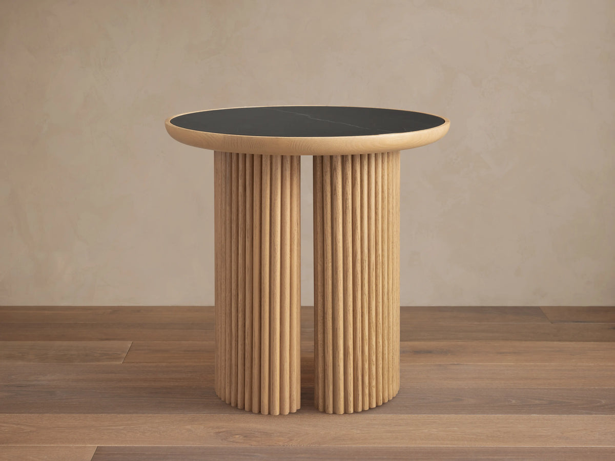 Astor Round End Table with a black marble tabletop and cylindrical oak reed-wrapped base on a wooden floor.