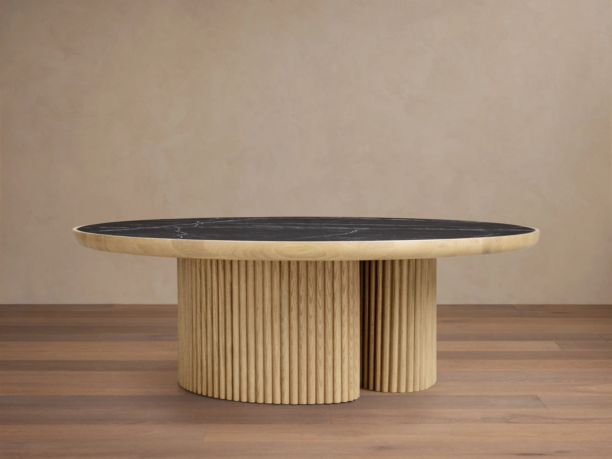 Astor Round Coffee Table with ribbed oak-wrapped wood veneer base and black natural marble top, on wooden floor.