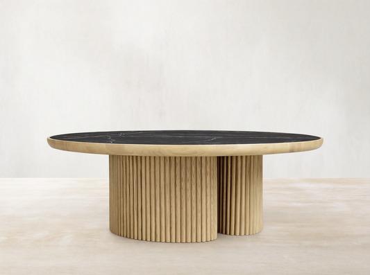 Astor Round Coffee Table with ribbed oak-wrapped wood veneer base and black natural marble top, on wooden floor.