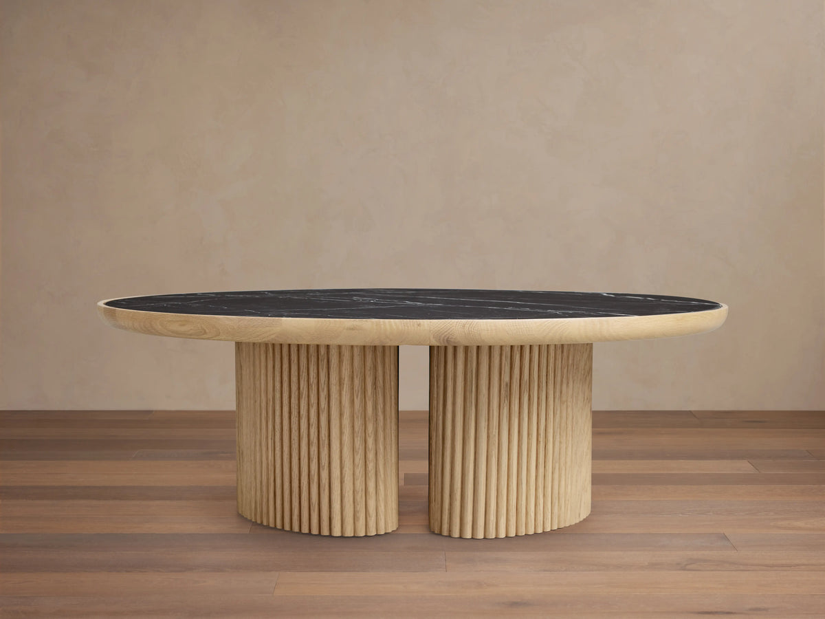 Astor Round Coffee Table with ribbed oak-wrapped wood veneer base and black natural marble top, on wooden floor.