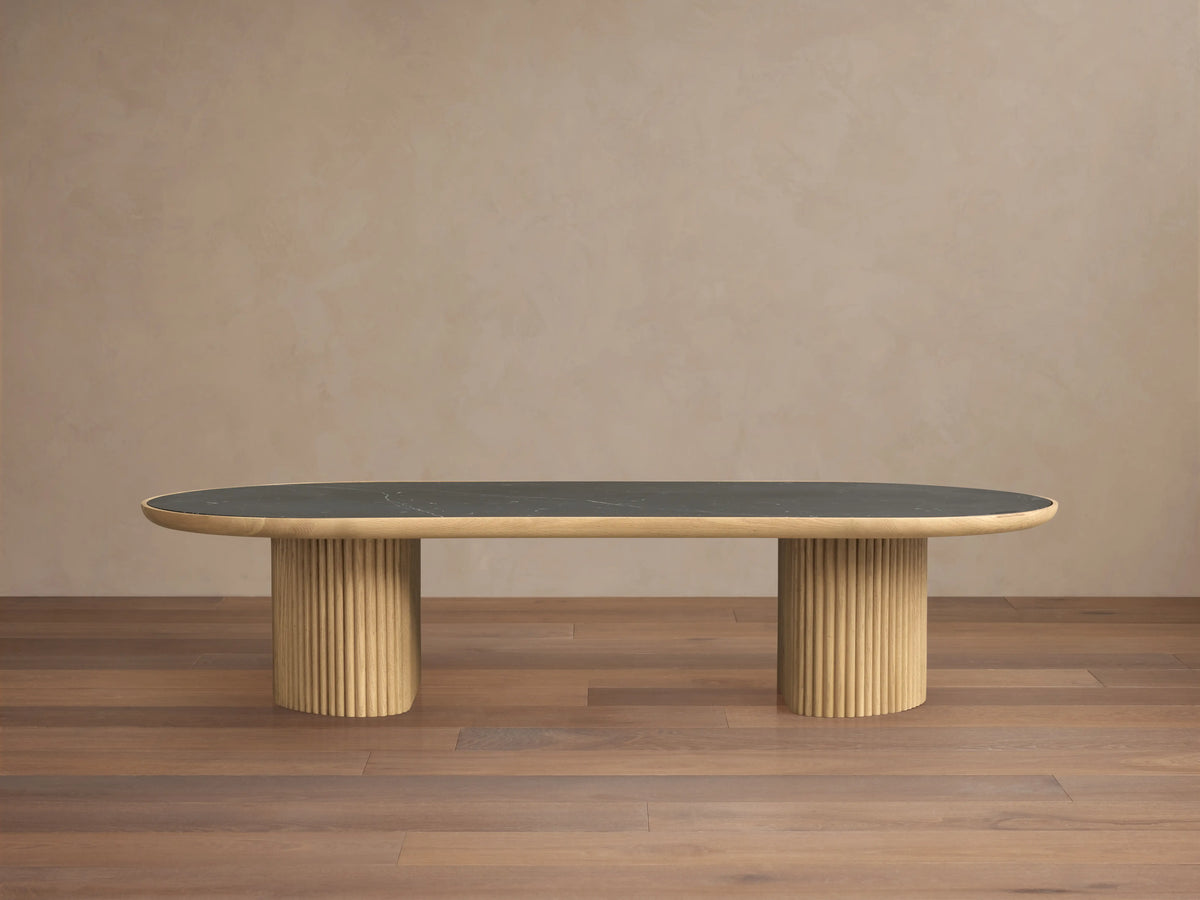 Astor Coffee Table with an oval marble top, supported by two cylindrical wooden bases wrapped in oak reeds, against a wooden floor.