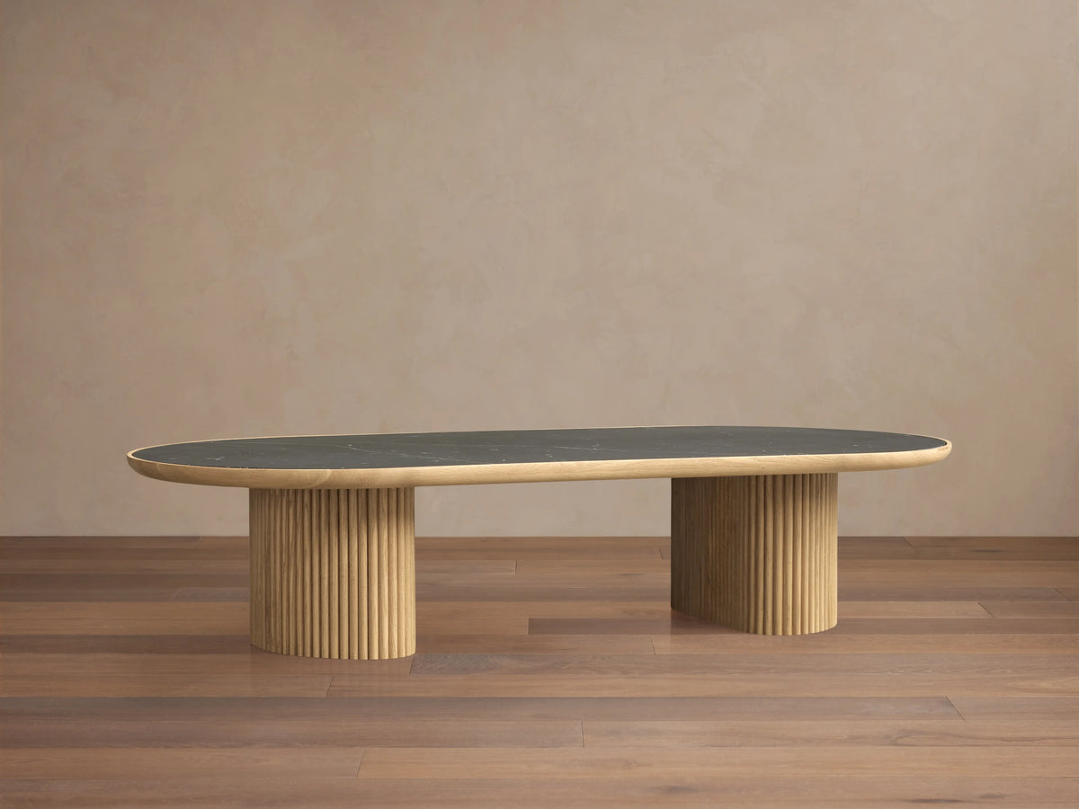 Astor Coffee Table with an oval marble top, supported by two cylindrical wooden bases wrapped in oak reeds, against a wooden floor.